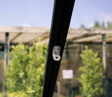 Close-up of metal hanging bracket attached to black frame with blurred outdoor garden background